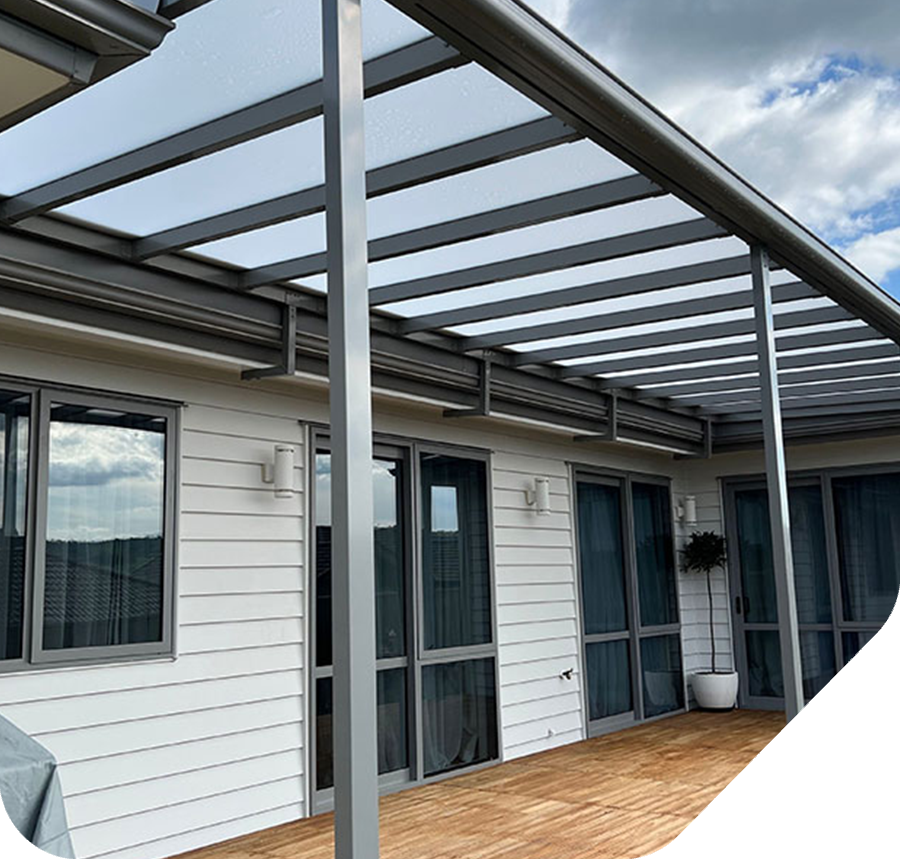 Pergola attached to a white house with gray trim. Wooden deck and clear roof panels.