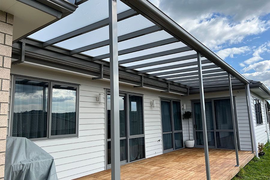 A gray patio cover extends from a white house, over a wooden deck.