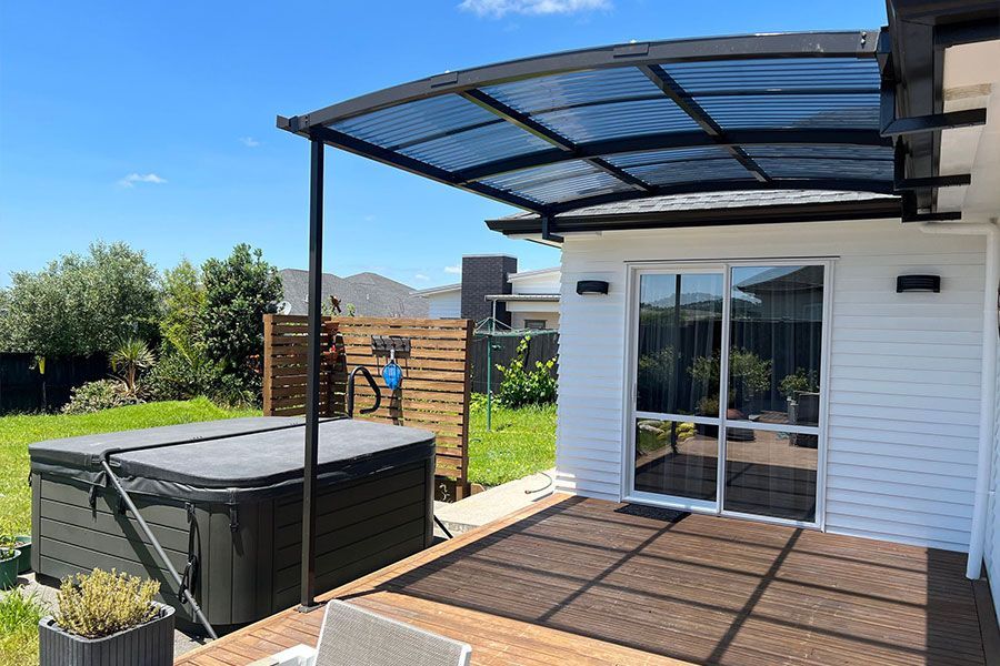 A backyard deck with a black hot tub and a covered patio on a sunny day.