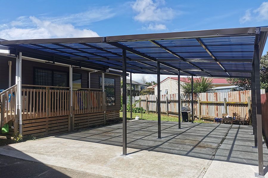 Carport attached to a house with a blue translucent roof, on a concrete patio.