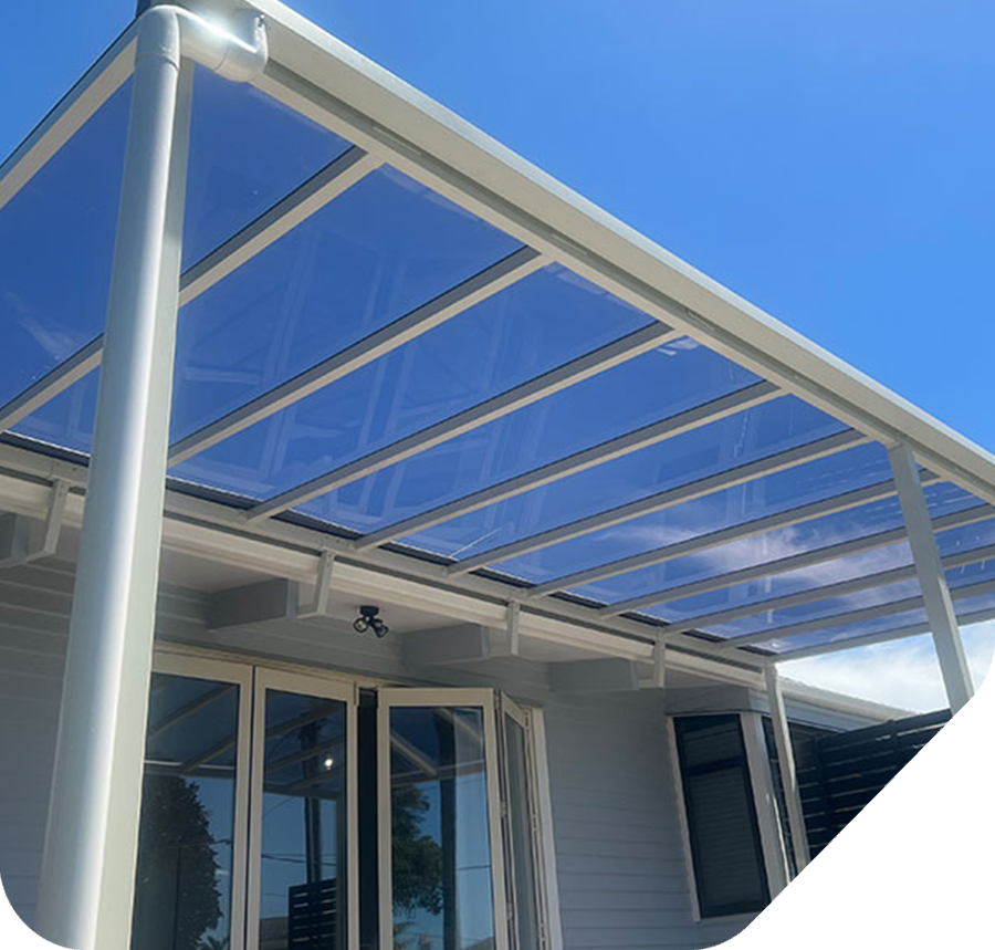 White framed patio roof with transparent panels over doors and windows, clear blue sky.