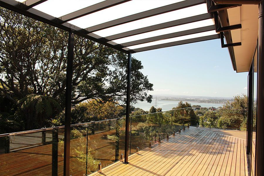 Wooden deck with glass railings and overhead canopy, overlooking a scenic view of the water and trees.