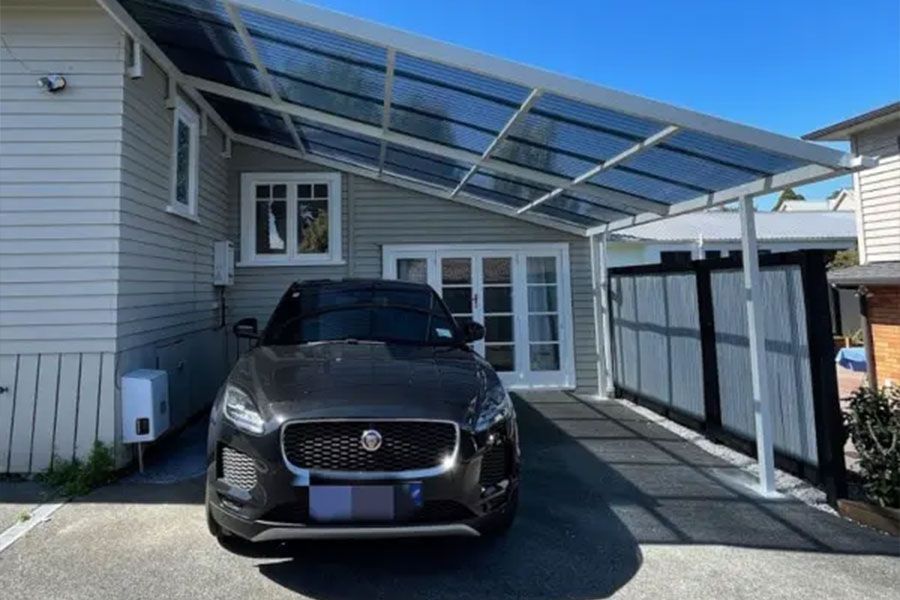 Black car parked under a carport attached to a gray house with a black gate.