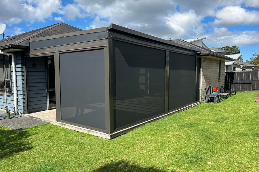 Enclosed patio with dark grey screens, next to a house on a green lawn.