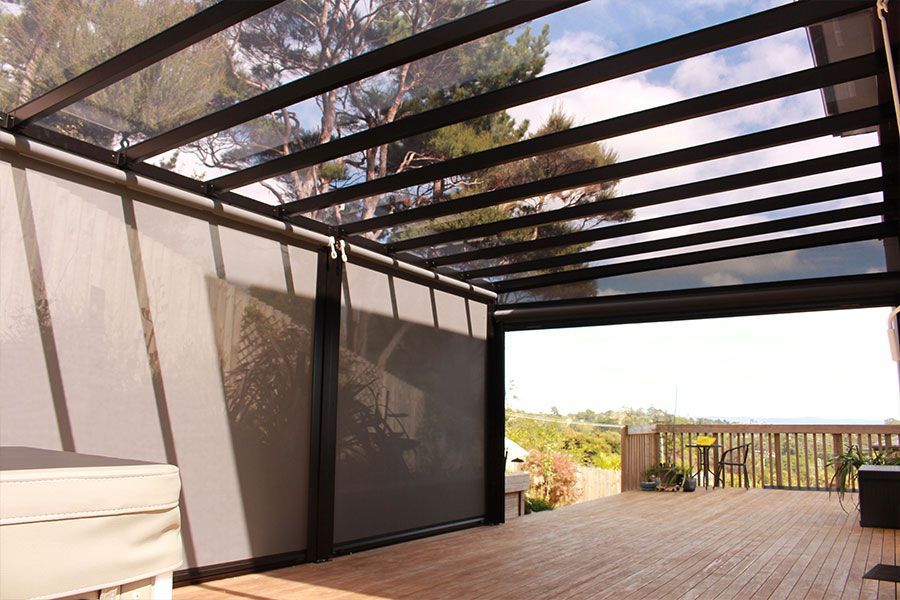 A modern deck with a black pergola, retractable shades, and a view of a tree-lined landscape.