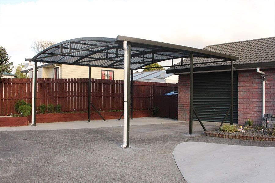 Carport with dark frame, attached to a brick building, over a driveway.