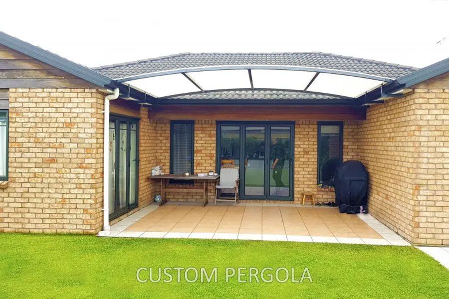Brick home with an attached pergola over a patio. Green lawn in the foreground.