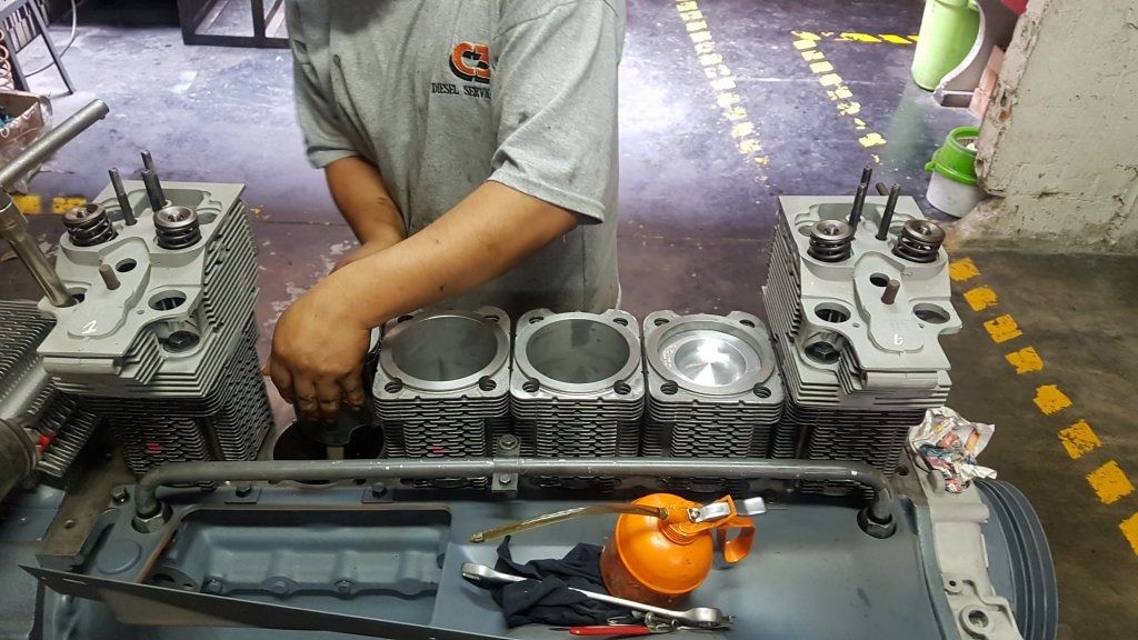 Motor de automóvil en taller con un mecánico trabajando en el bloque de cilindros y herramientas cerca.