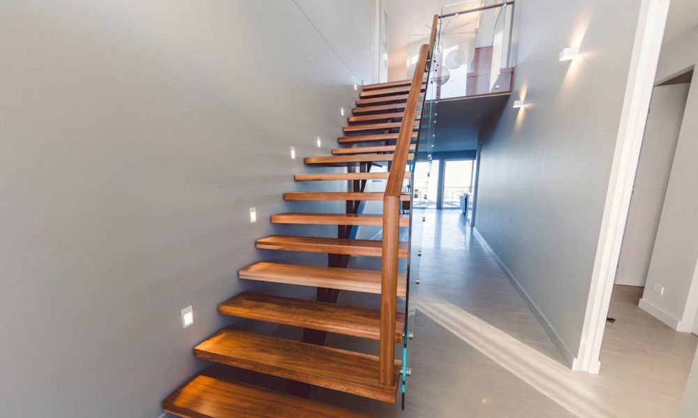 A Wooden Staircase With a Glass Railing in a Hallway in a House — QBC Constructions In Shellharbour, NSW