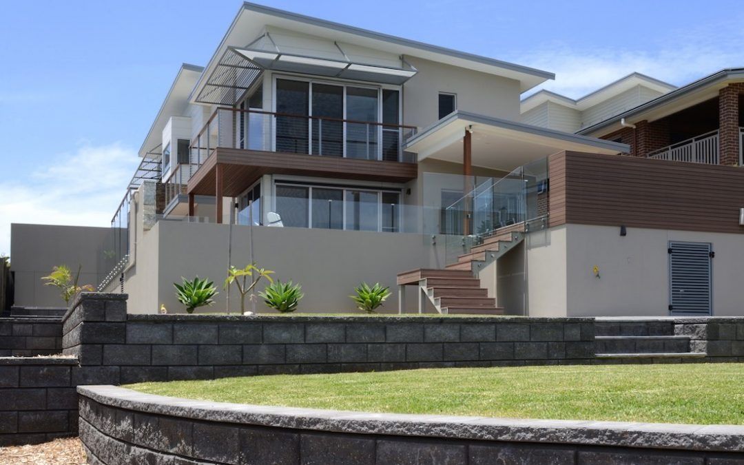 A Large House With Stairs Leading Up To It Is Sitting On Top Of A Lush Green Hillside — QBC Constructions In Werri Beach, NSW