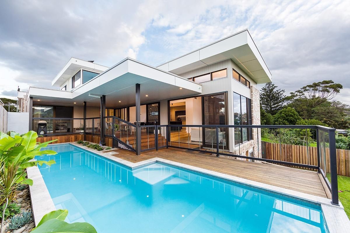 A Modern House With A Large Swimming Pool In Front Of It — QBC Constructions In Kiama, NSW