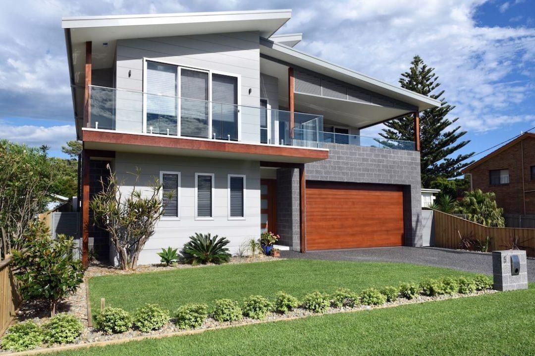 A Large House With A Wooden Garage Door And A Large Lawn In Front Of It — QBC Constructions In Kiama, NSW