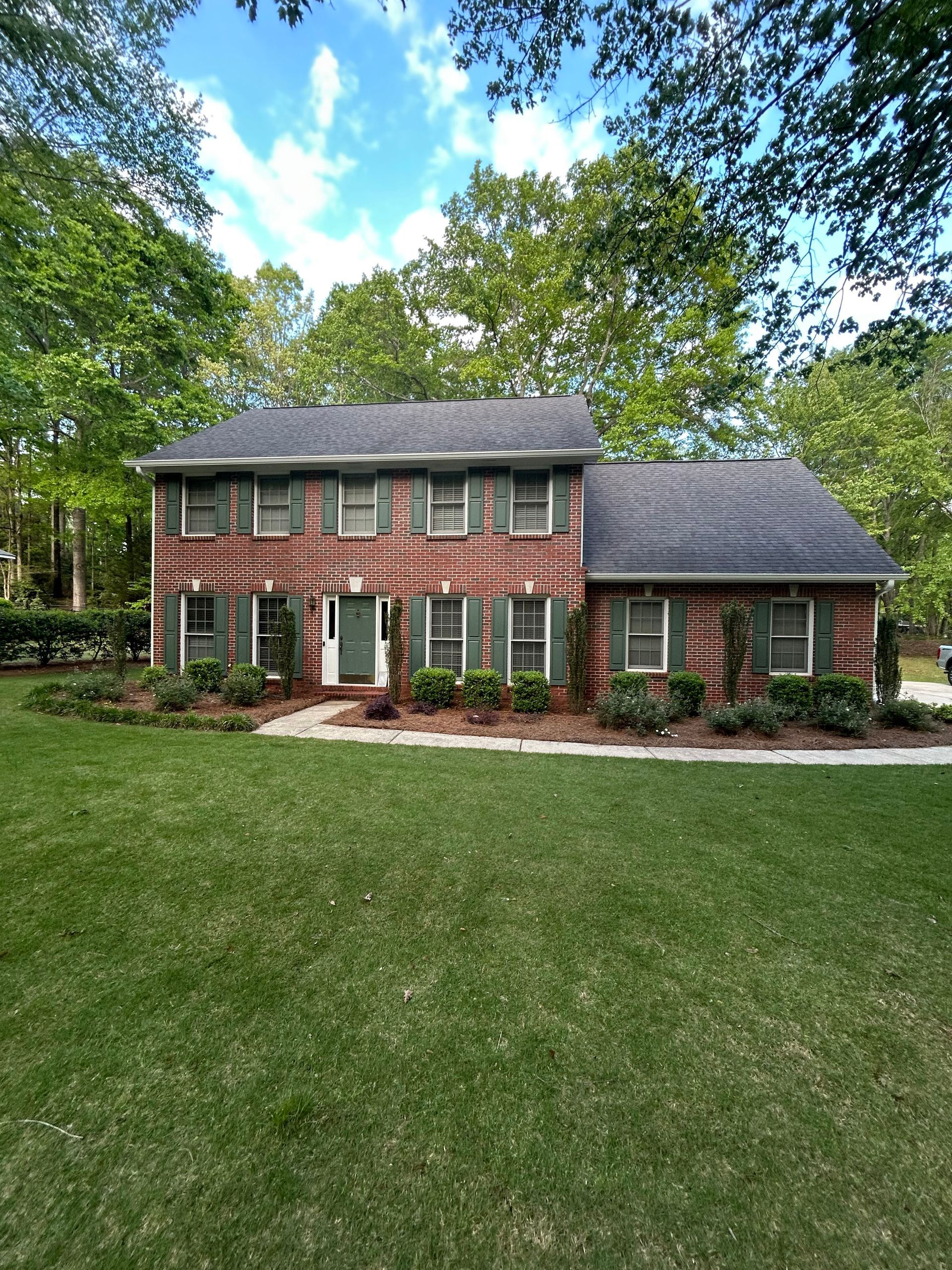 A large brick house with green shutters and a lush green lawn in front of it.