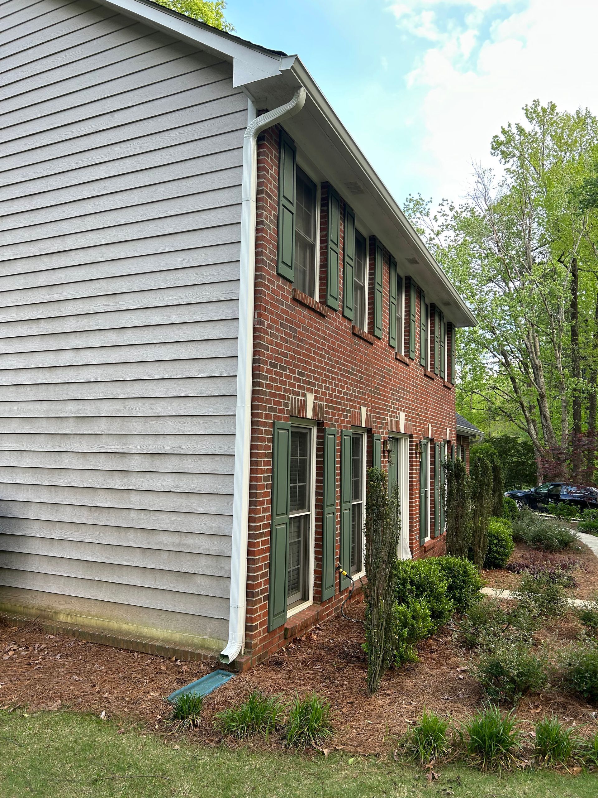 A brick house with a white siding and green shutters.