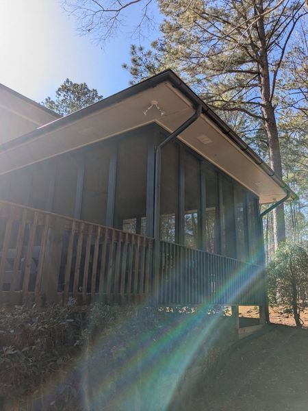 A house with a screened in porch and trees in the background.