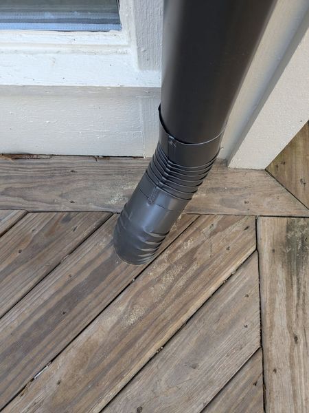 A black pipe is sitting on a wooden deck next to a window.