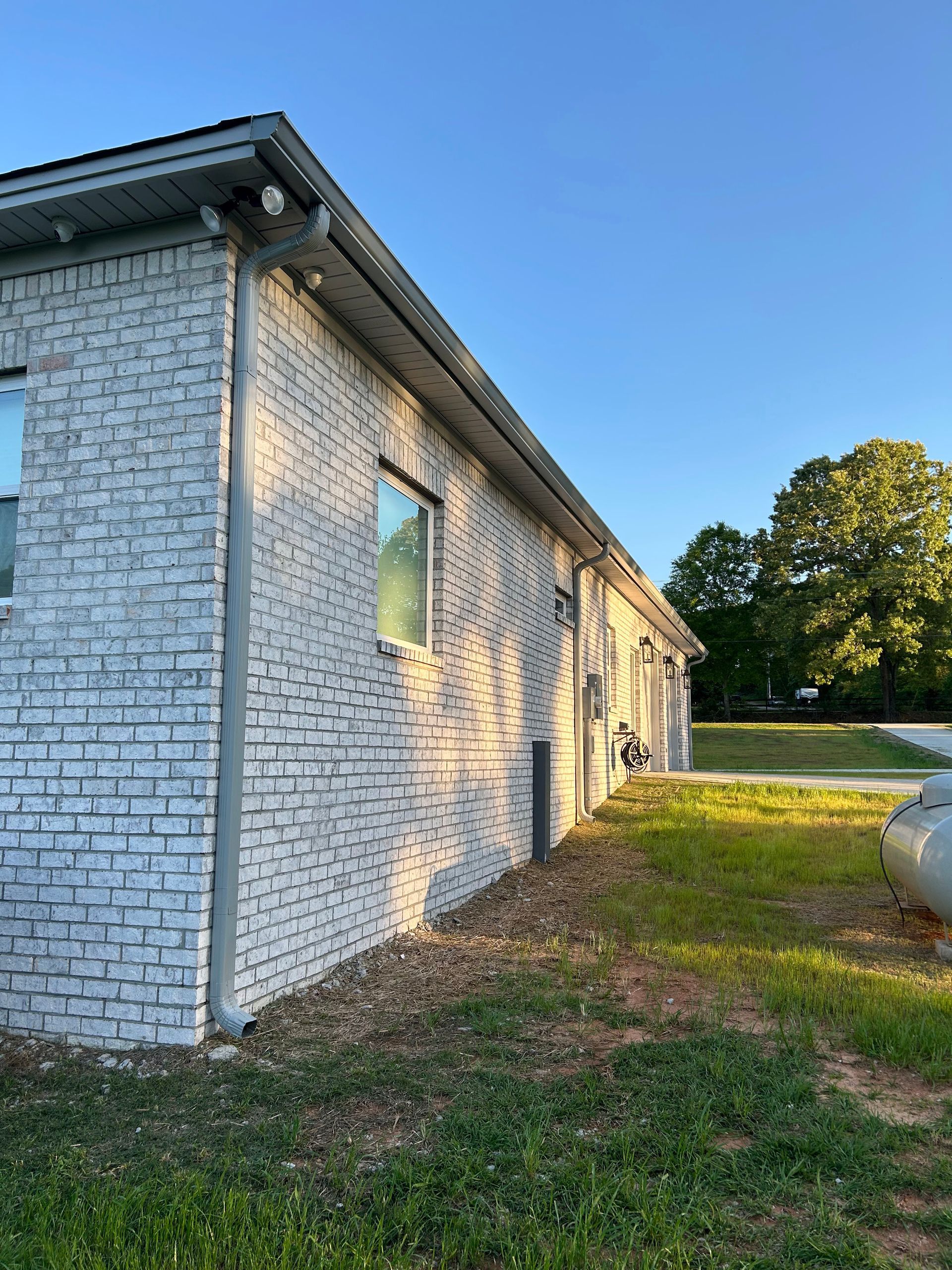 A white brick building is sitting in the middle of a grassy field.
