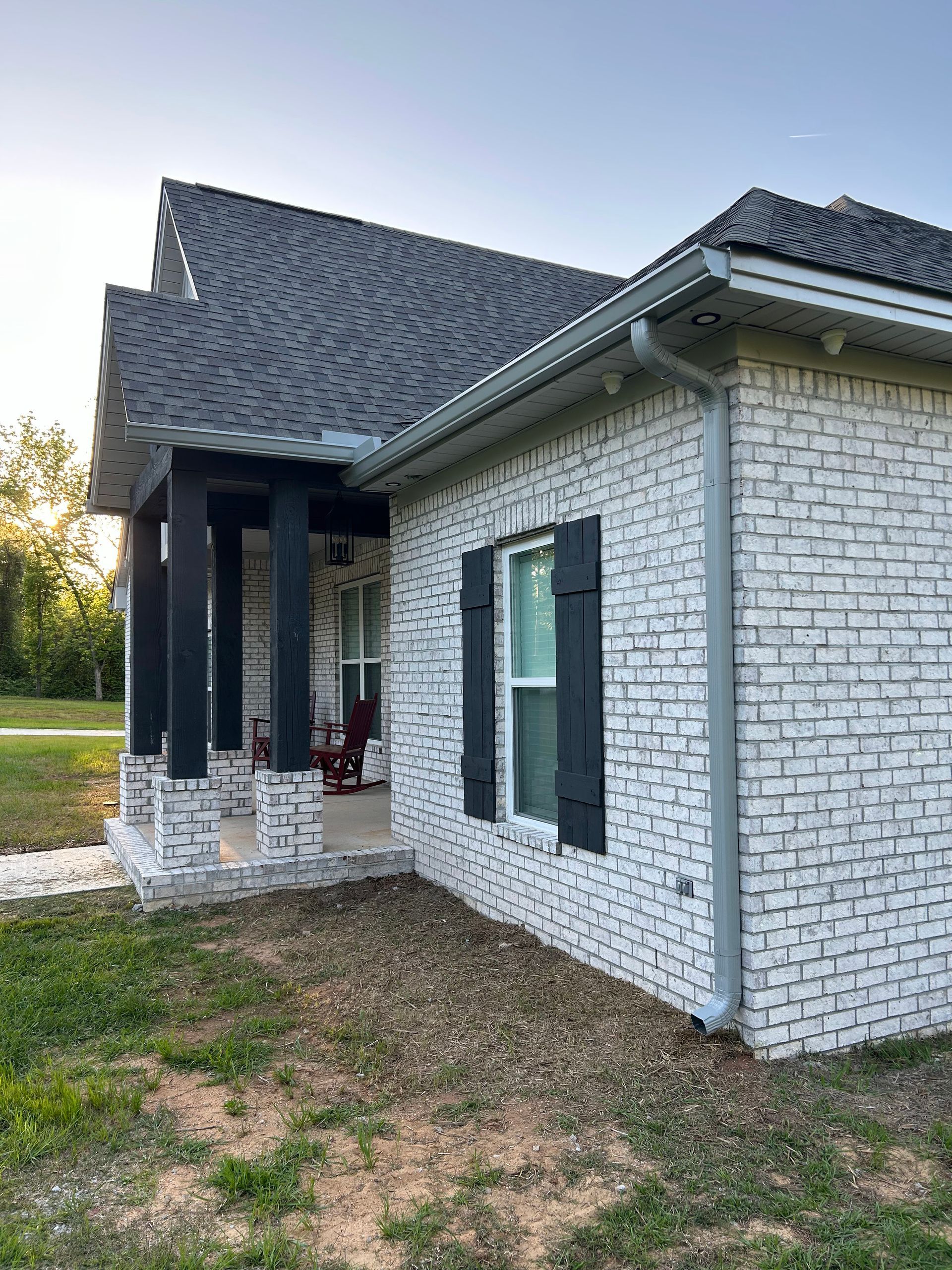 A white brick house with black shutters and a porch.