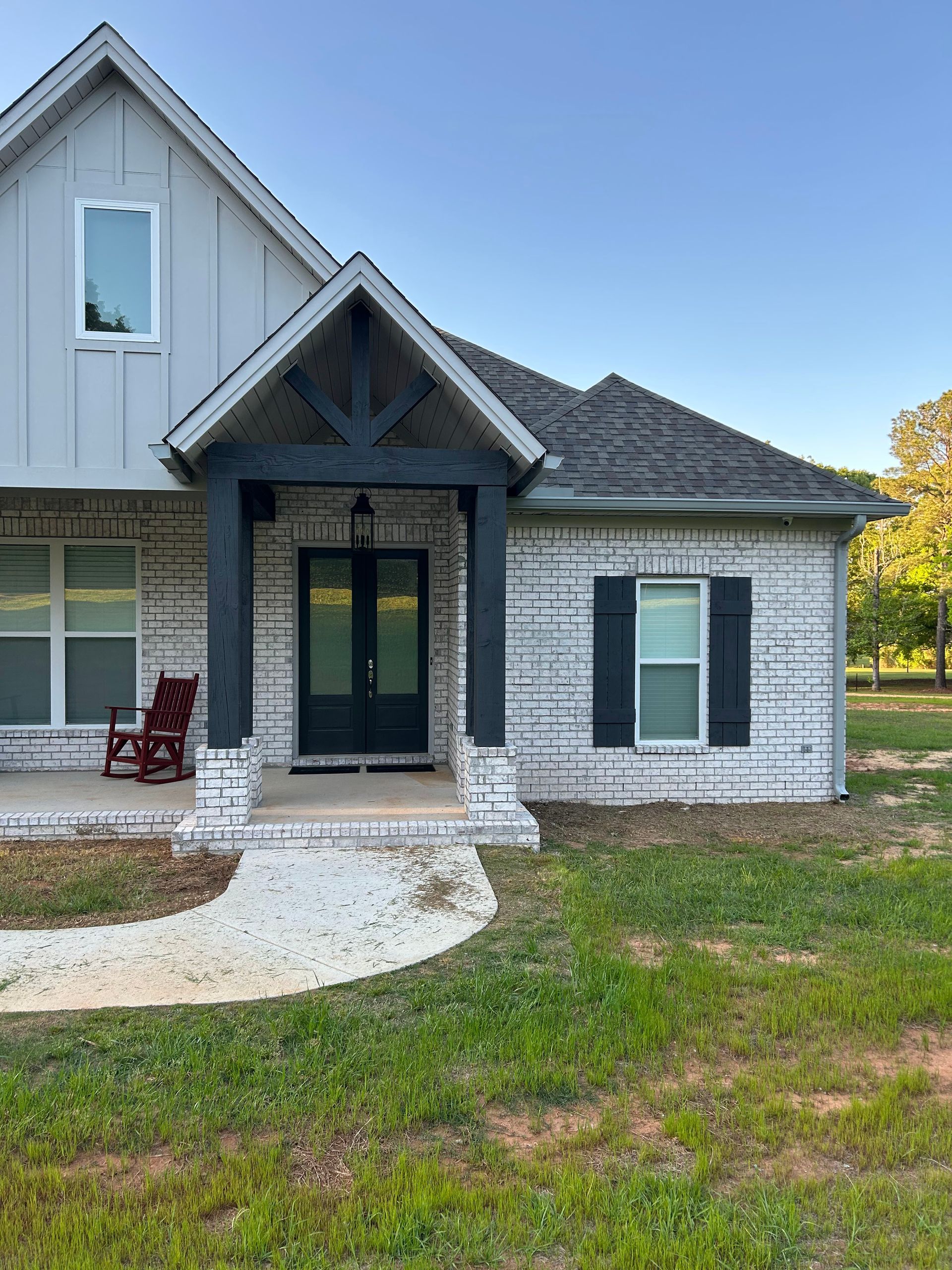 A white brick house with black shutters and a red rocking chair on the porch.