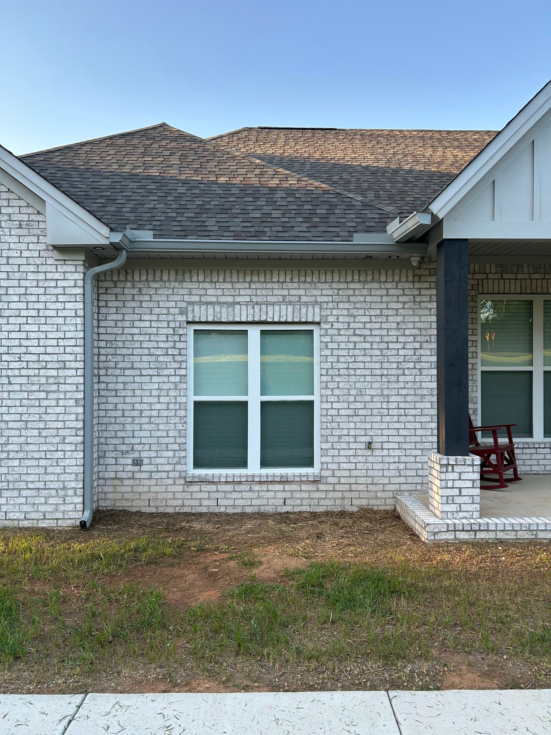 A white brick house with a porch and a rocking chair in front of it.