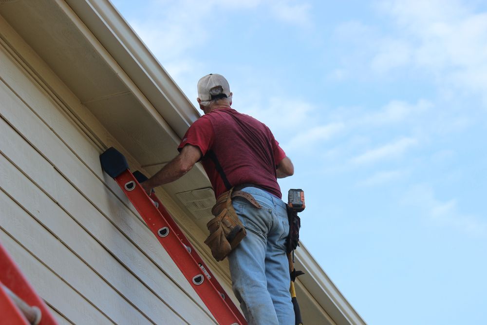 A man is standing on a ladder on the side of a house.