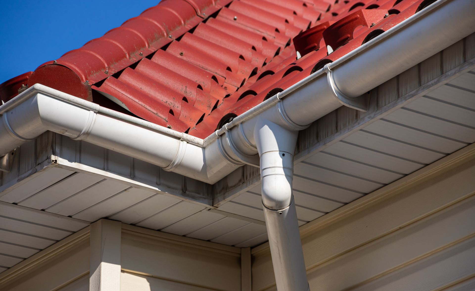 A White Gutter on the Side of a House With a Red Roof