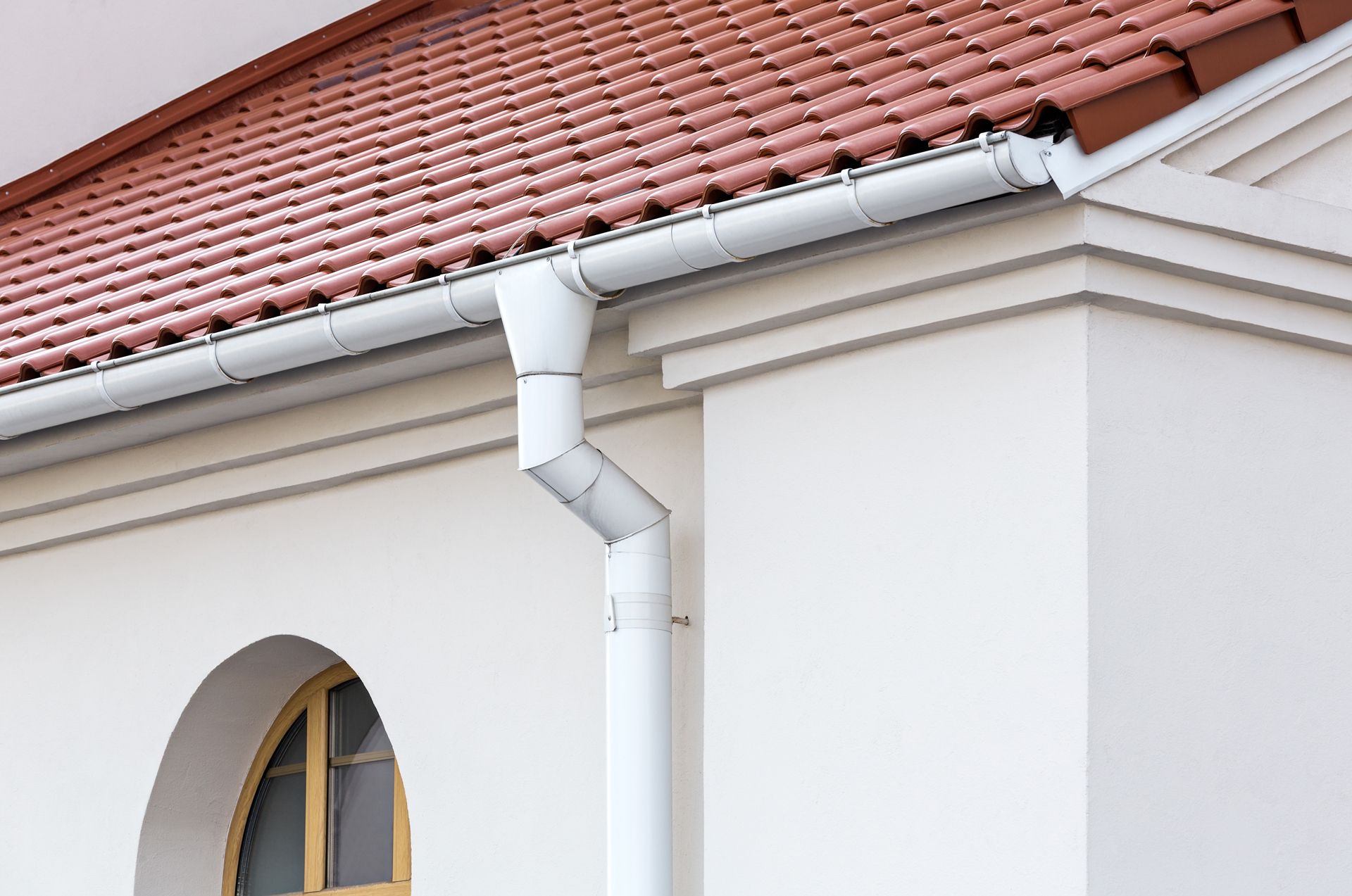 A White Gutter on the Side of a Building With a Red Tile Roof
