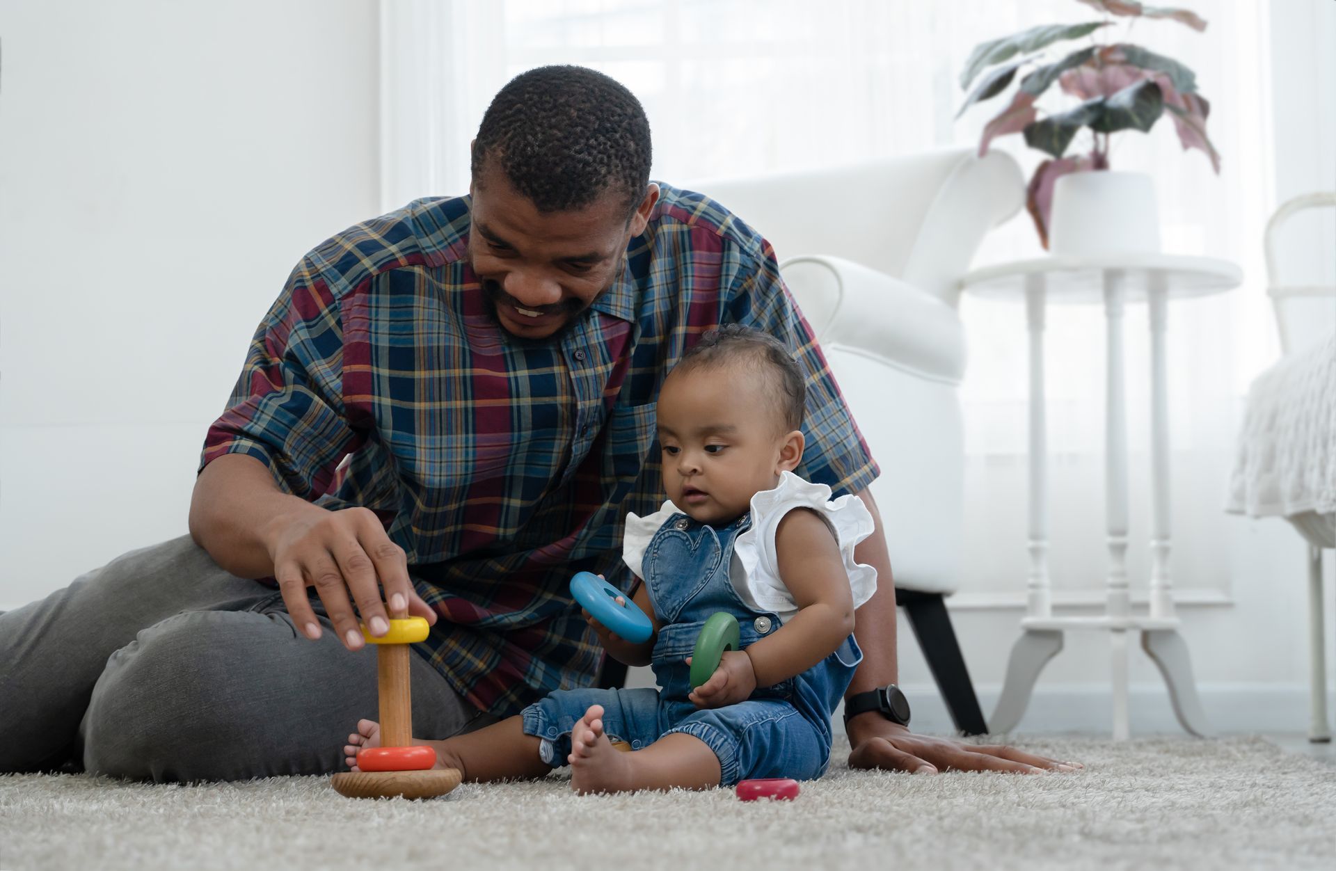 Person vacuuming a rug; dog watches from floor. Living room setting with sofa, pillows, and window.