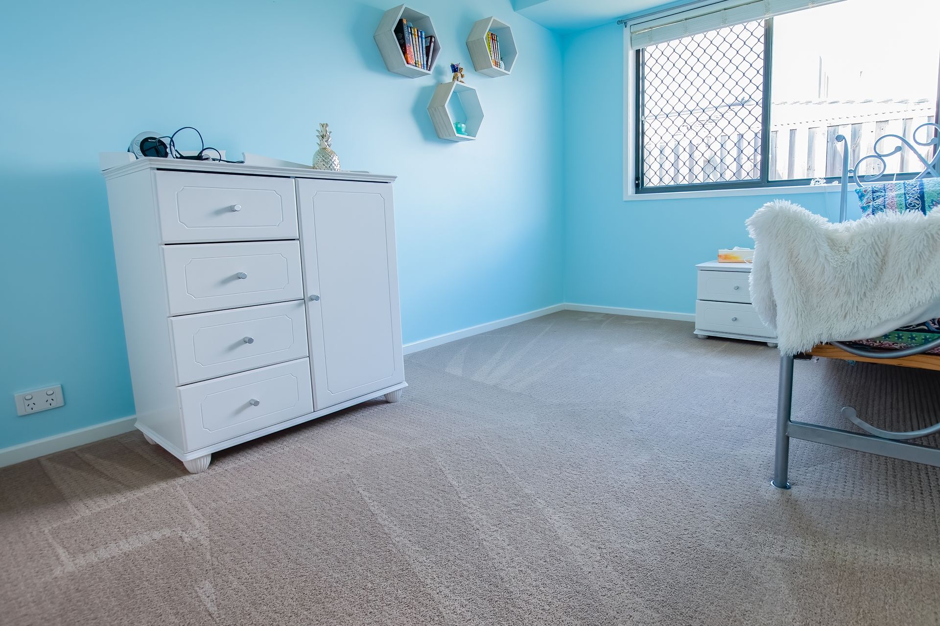 Three people in blue aprons cleaning a living room with white walls, a sofa, and vacuum cleaner.