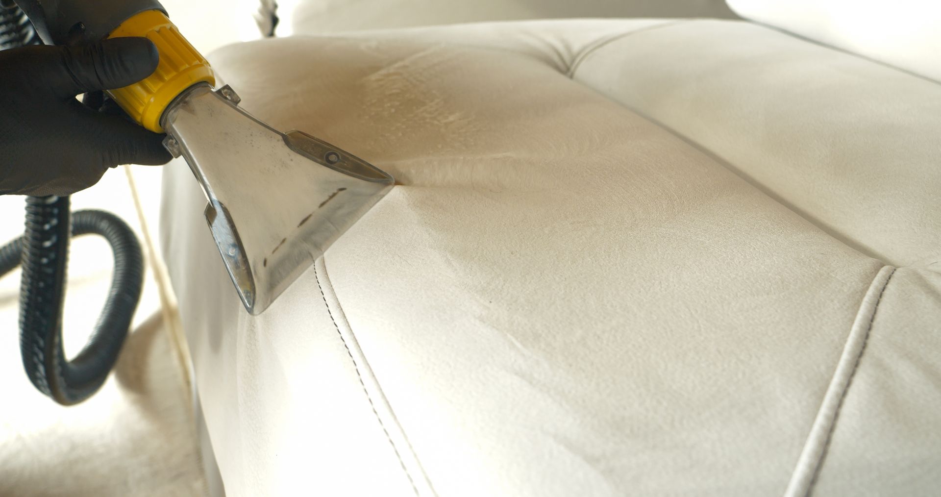 Person vacuuming a blue couch with yellow pillows in a living room.