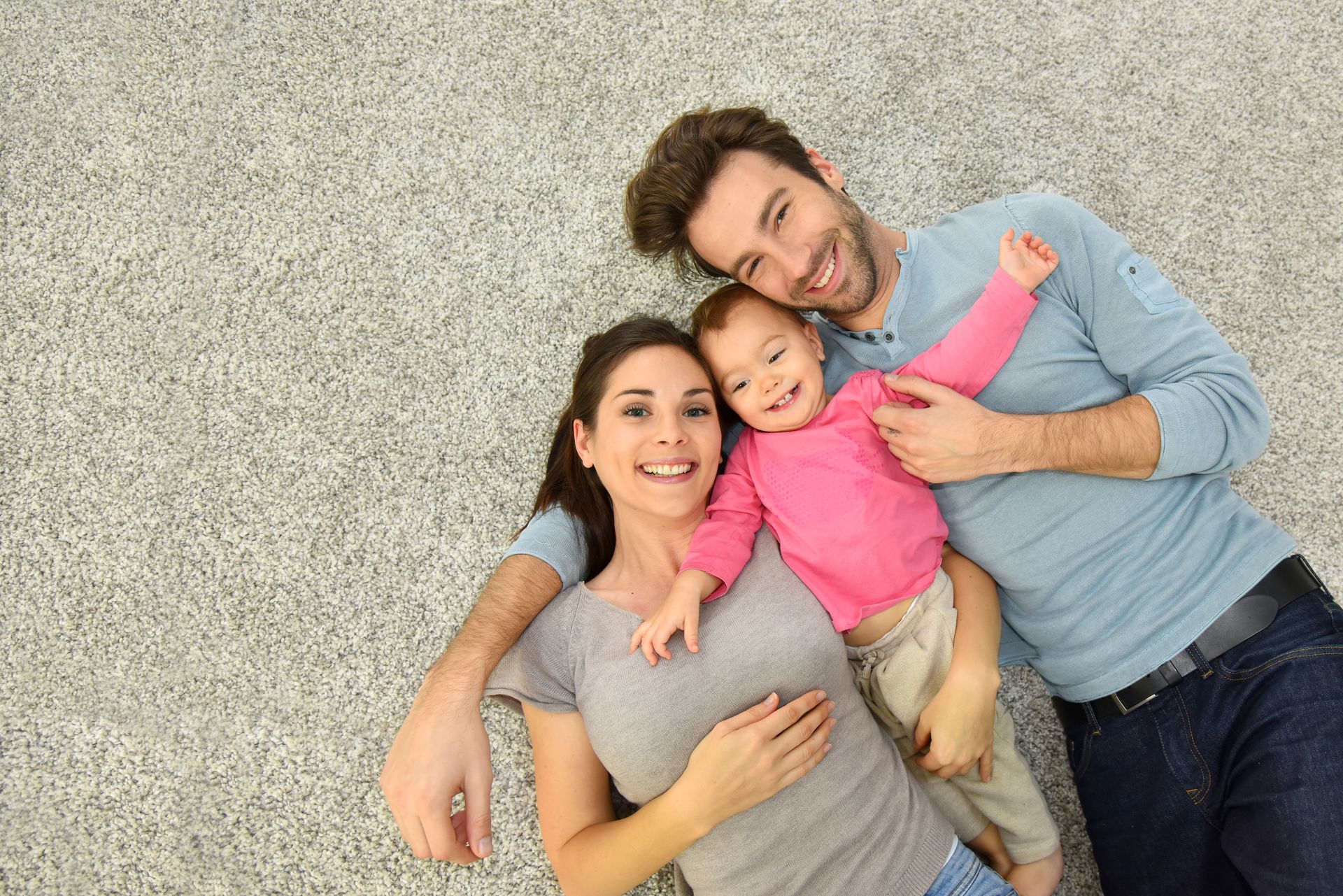 Three people in blue aprons cleaning a living room with white walls, a sofa, and vacuum cleaner.