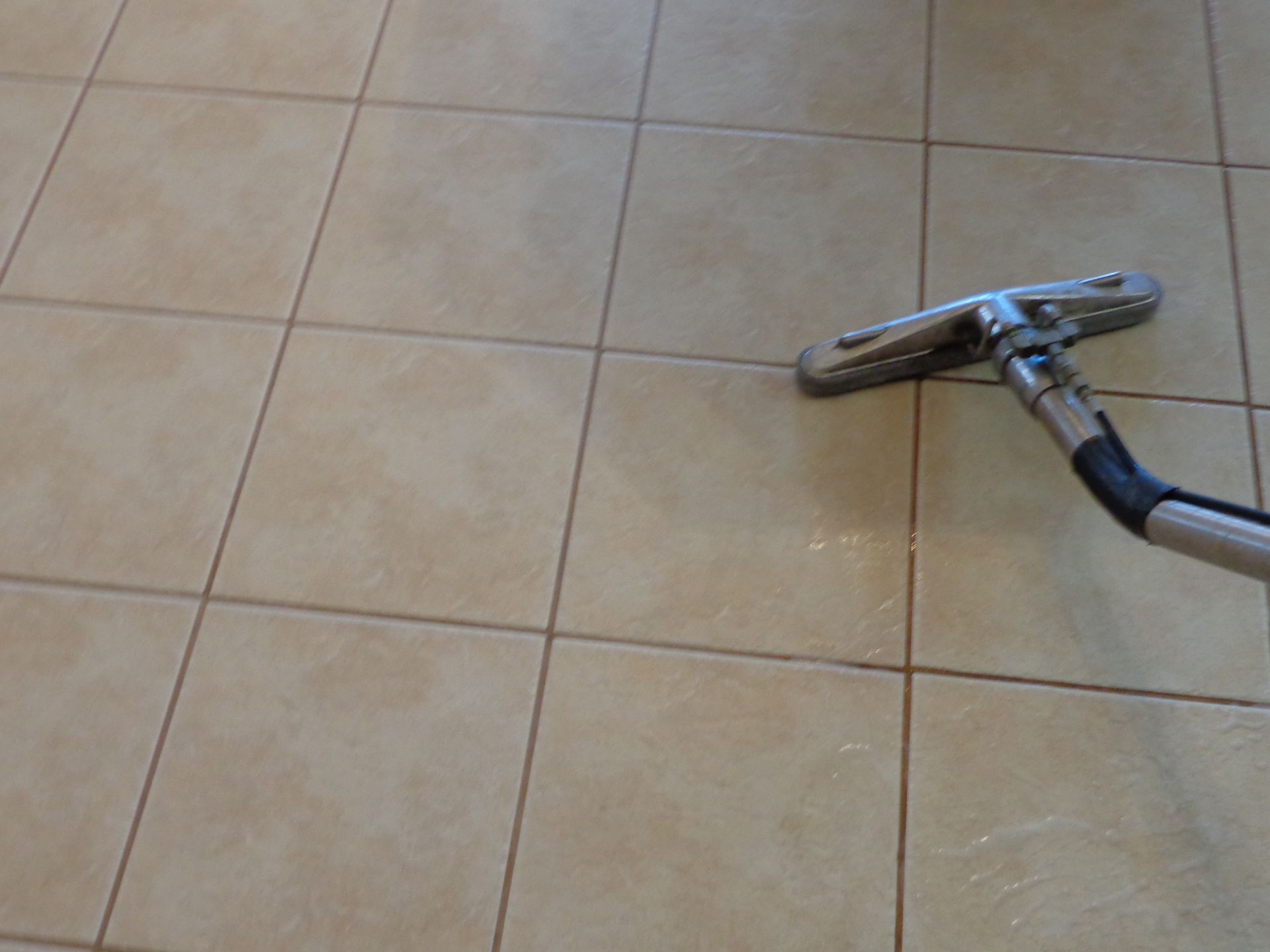 Person in gloves steam-cleaning white tiled backsplash with a black and yellow device; steam visible.