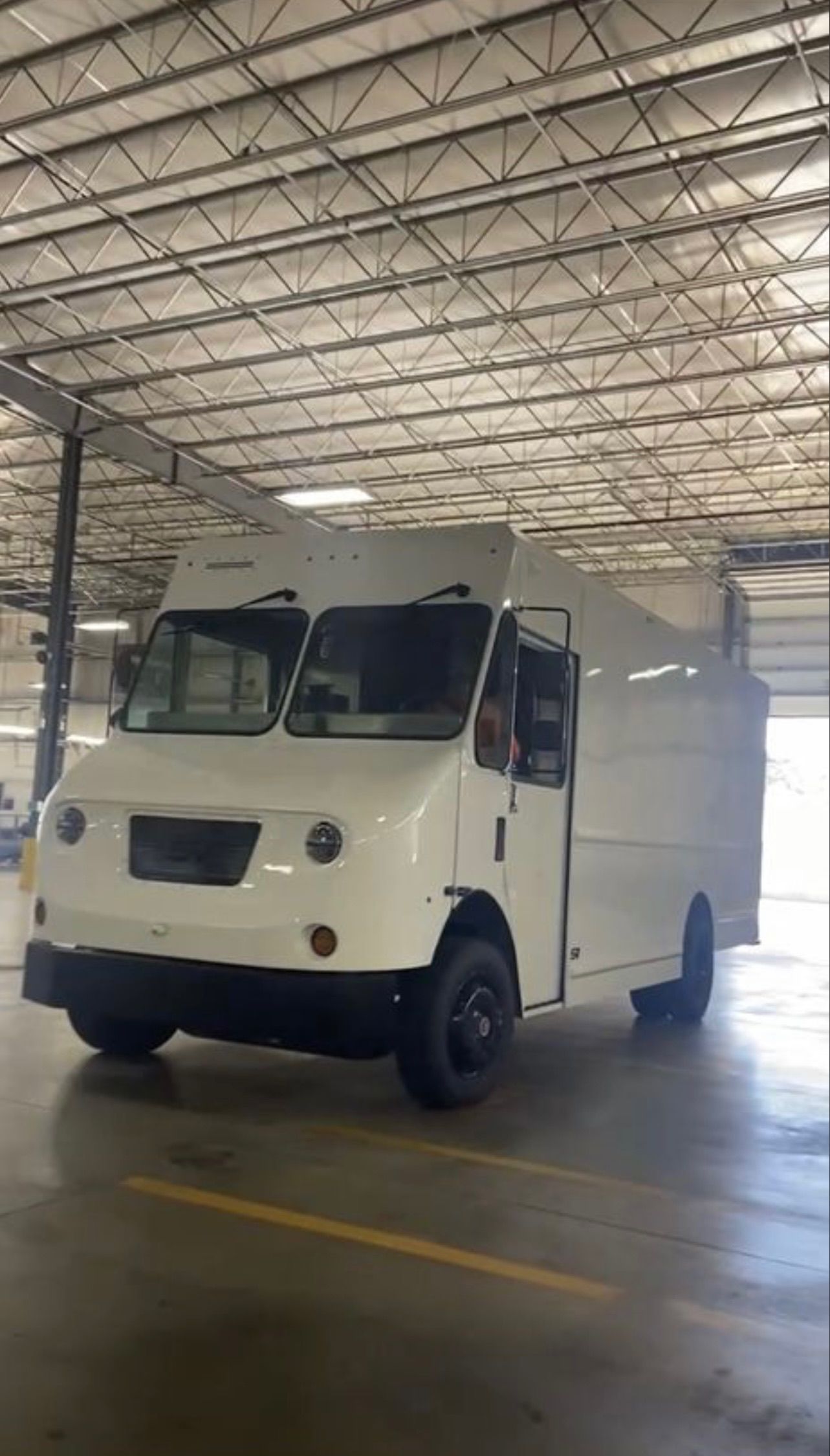 A white delivery truck parked inside a warehouse. The truck is boxy with black tires.