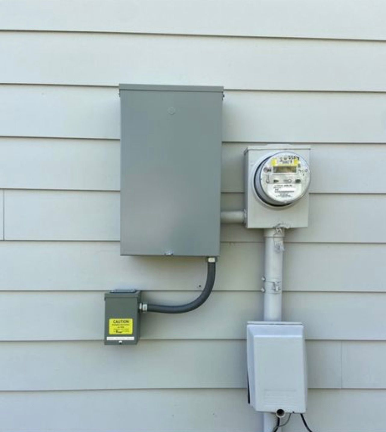 Electrical meter and panel on a gray-sided house. Gray metal box contains the breaker pane