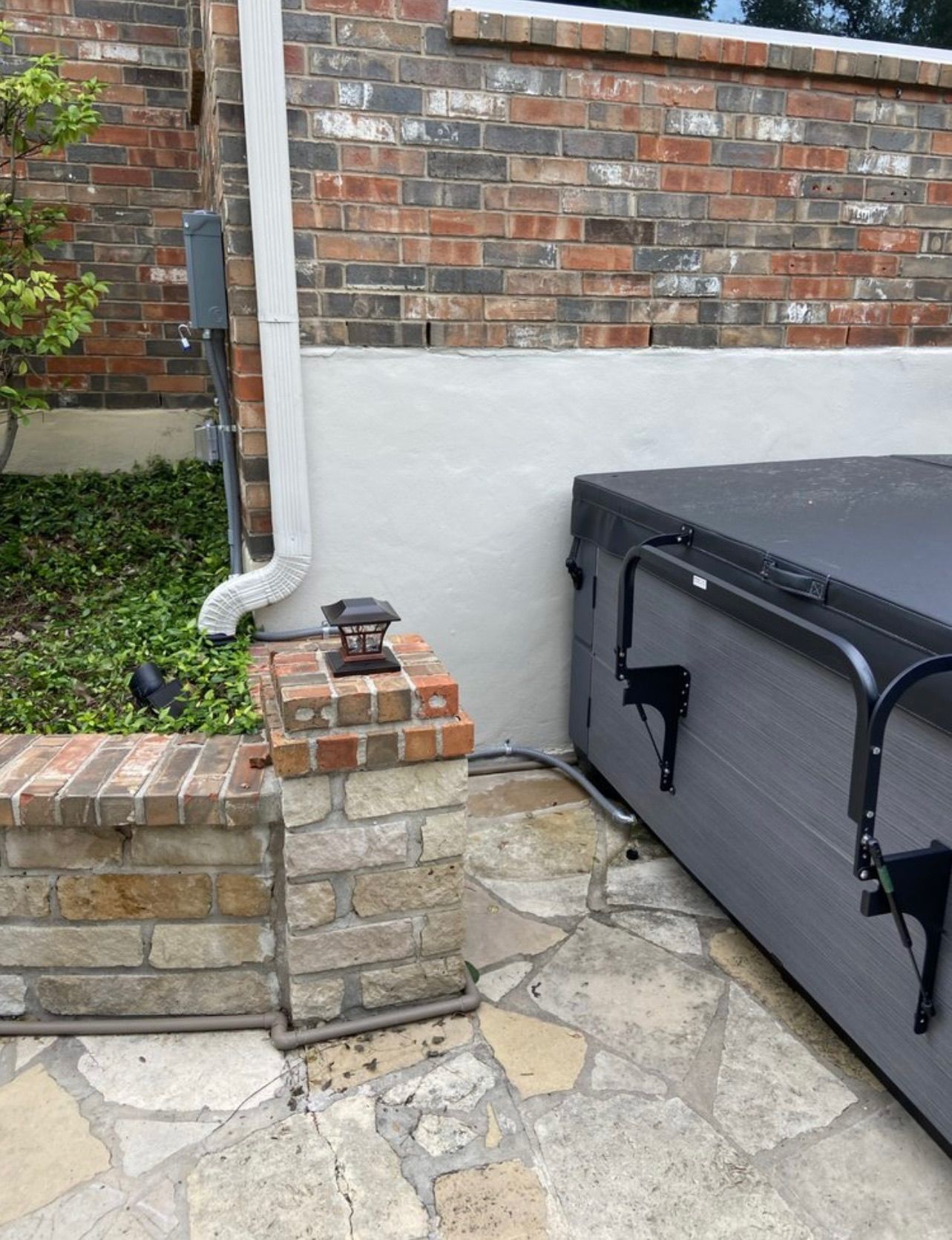 Backyard scene with brick wall, stone patio, and a hot tub. A downspout runs along the wall.