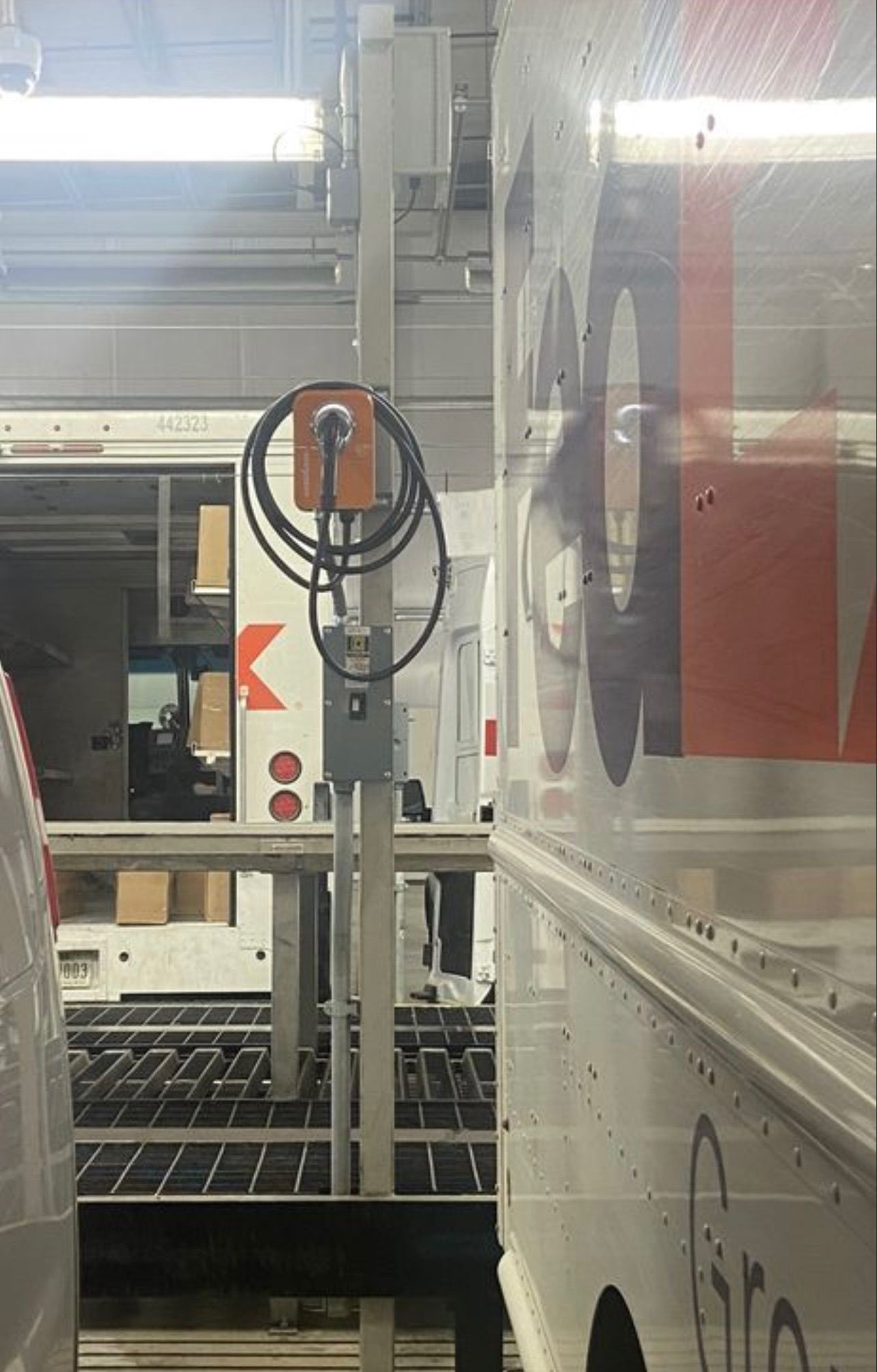 A power outlet on a pole between two delivery trucks inside a warehouse. The outlet is orange and black.