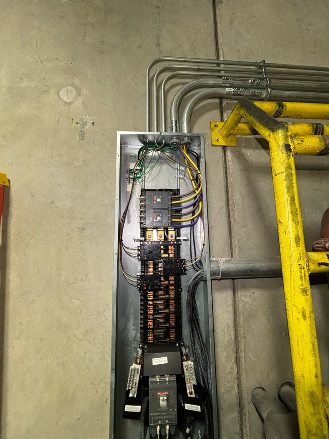 An electrician is working on a wiring box, stripping wires with orange pliers.