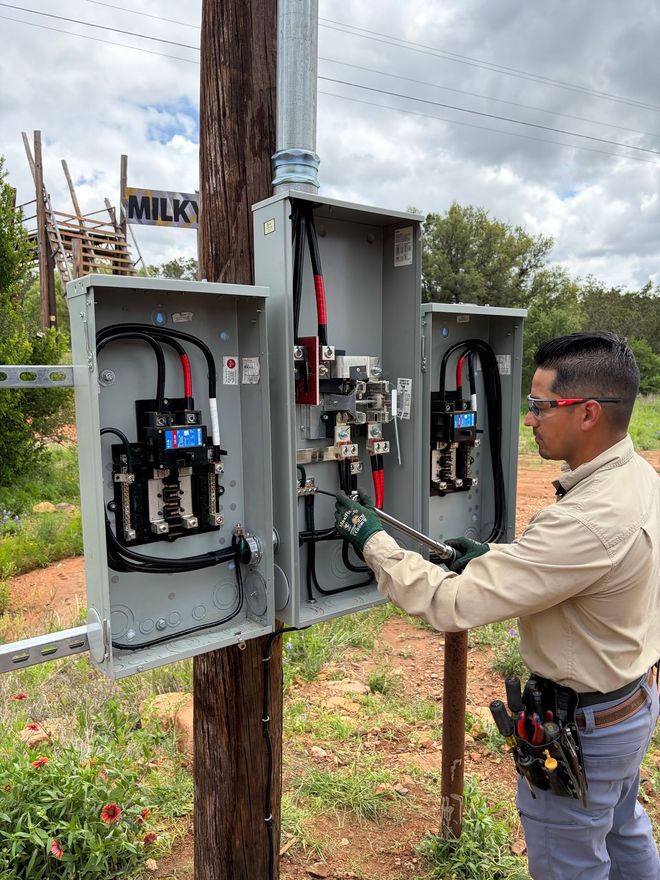 An electrician is working on a wiring box, stripping wires with orange pliers.