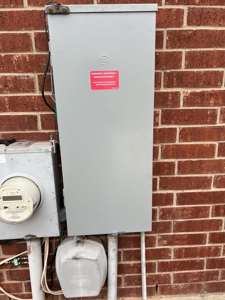 Exterior electrical panel and meter box on a red brick wall. Gray metal panel has a red warning label.