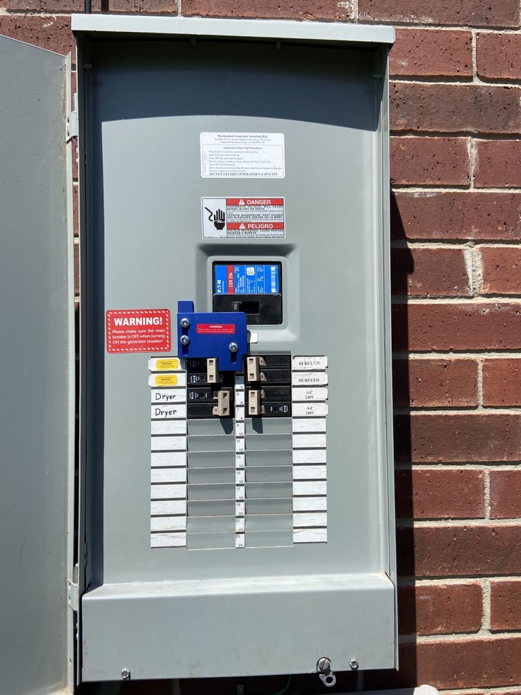 A gray electrical panel, mounted on a brick wall, with various switches, labels, and safety devices. The panel door is ajar.