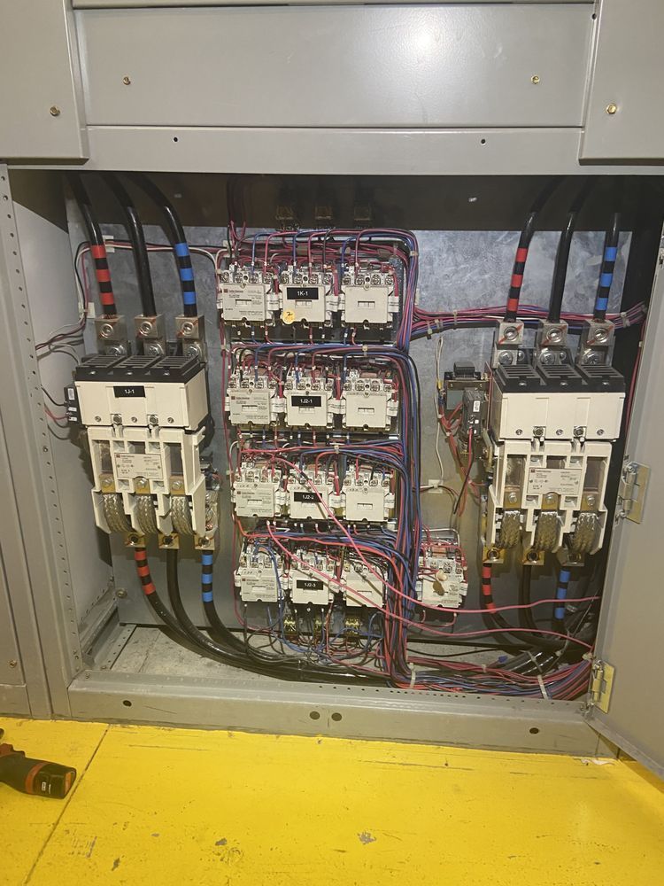 Electrical panel interior with numerous contactors, wires, and circuit breakers.