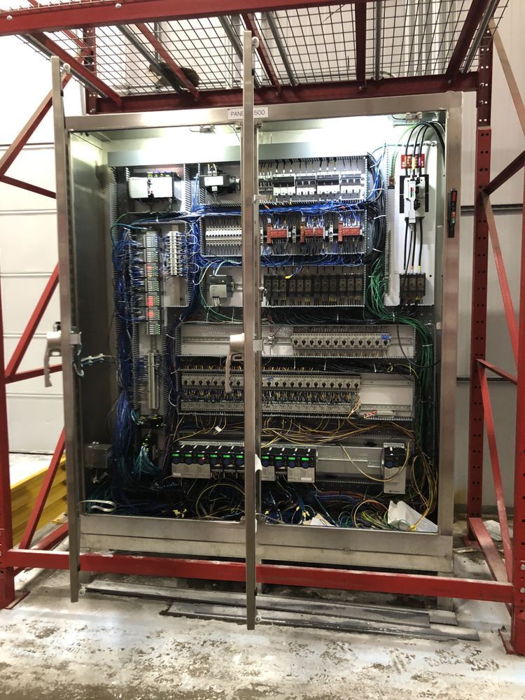 Electrical control panel with numerous wires and components, inside a metal frame structure,