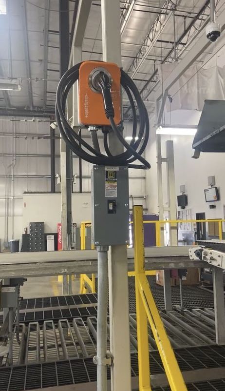 An orange power supply box and a gray electrical panel are mounted on a metal pole in an industrial setting.