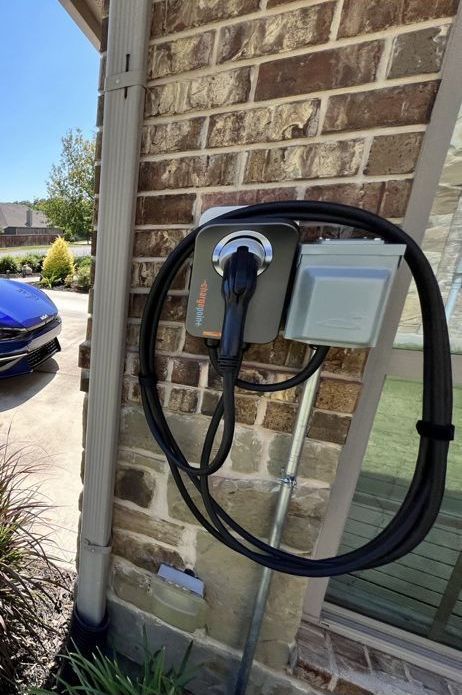 An electric vehicle charging station mounted on a brick wall next to a building's edge.