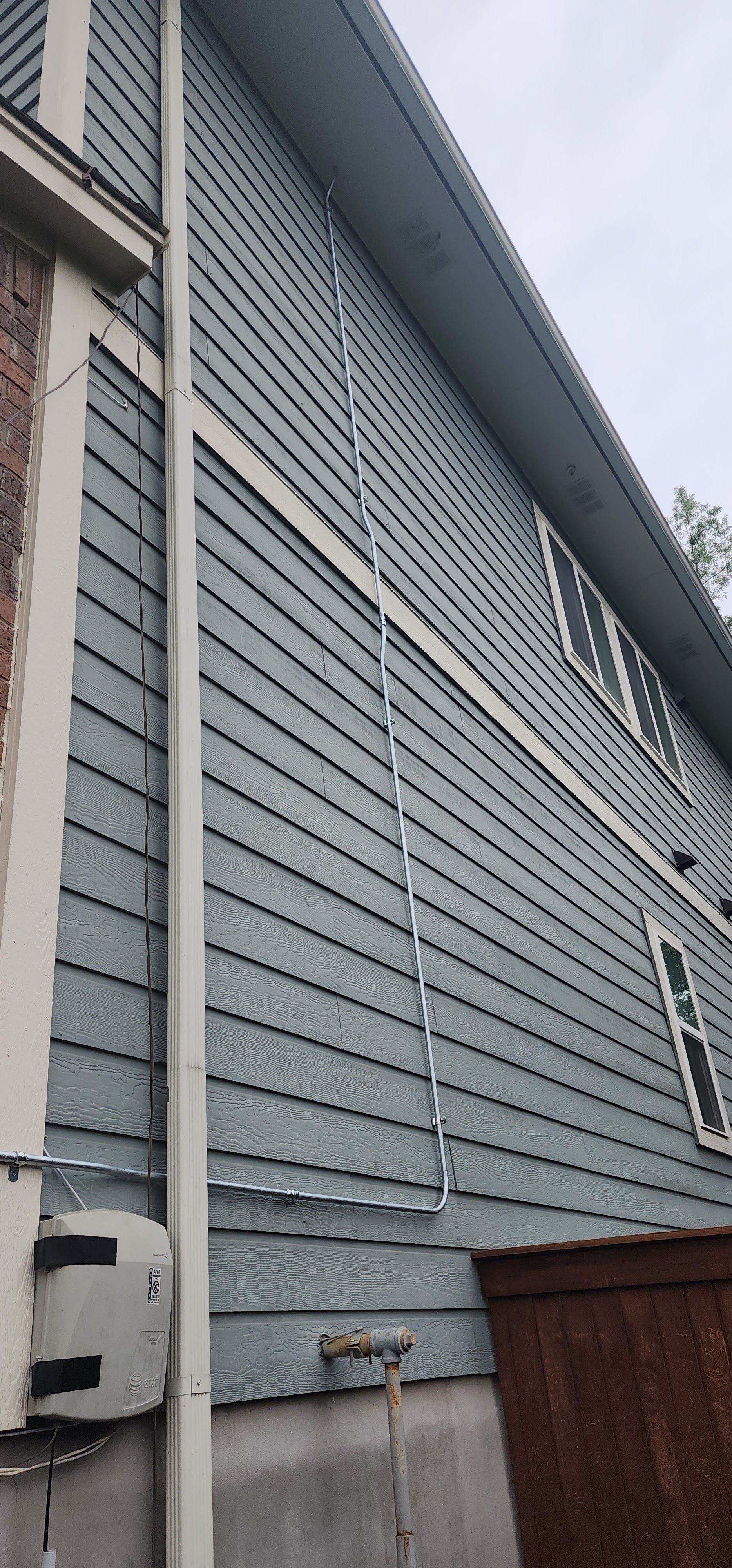 Exterior view of a house with gray siding, white trim, and a white downspout.