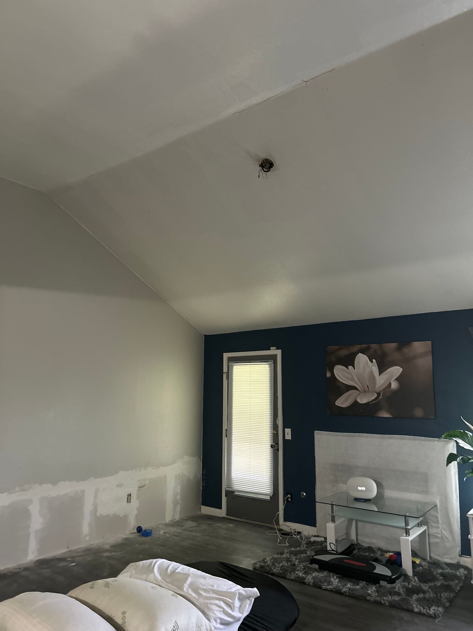 Interior of a room with a high ceiling, a dark blue accent wall, a closed door, and drywall on the bottom of the walls.