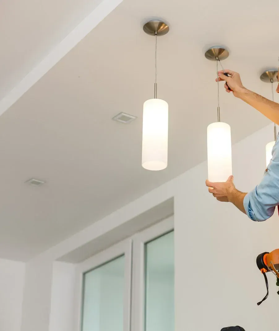 Person installing a pendant light fixture. The setting is an interior with white walls and a white ceiling.