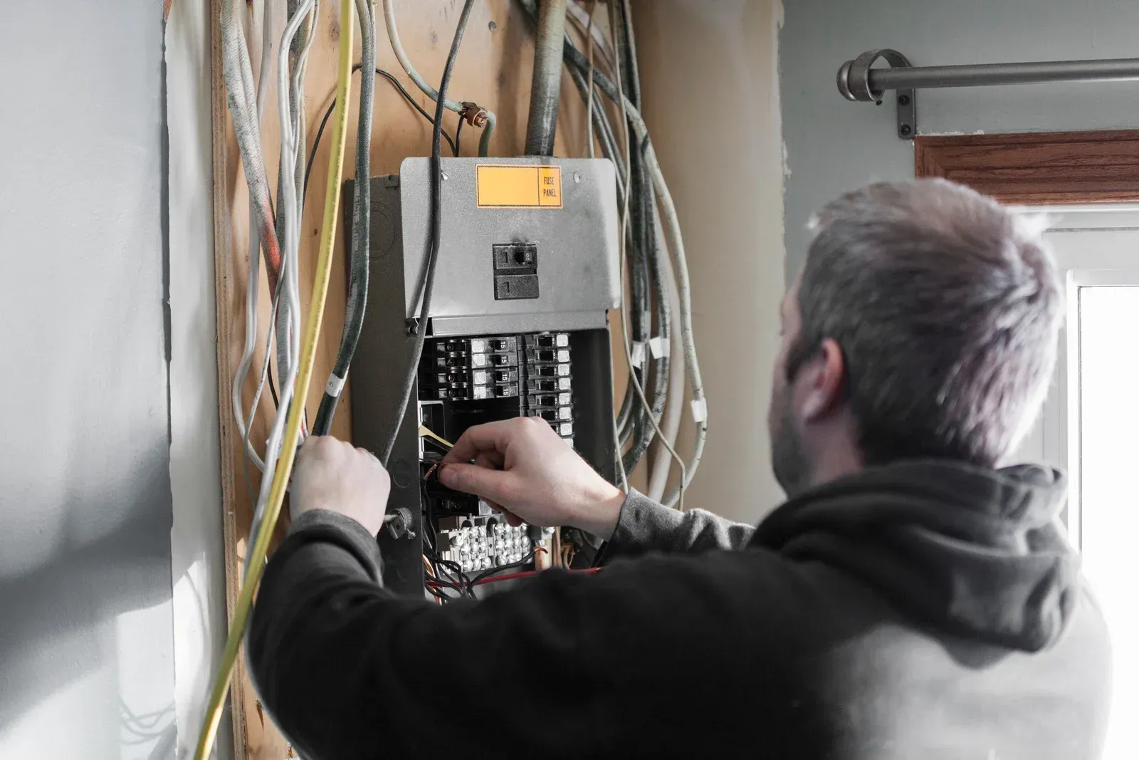 Electrician using a multimeter to test a fuse box, wearing white gloves. The meter reads 222 volts.
