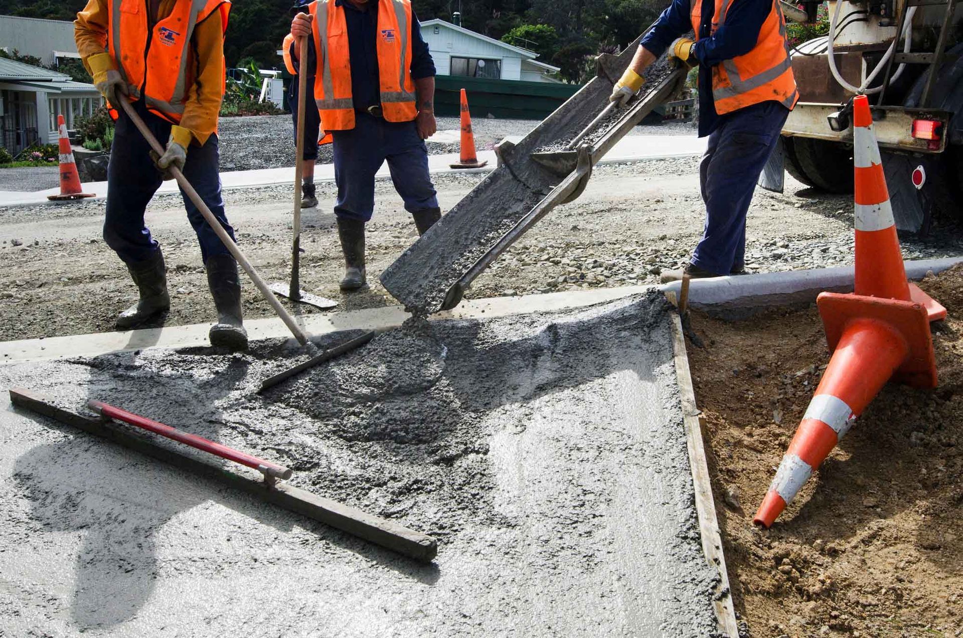 Construction workers in safety vests pouring and spreading concrete on a road.