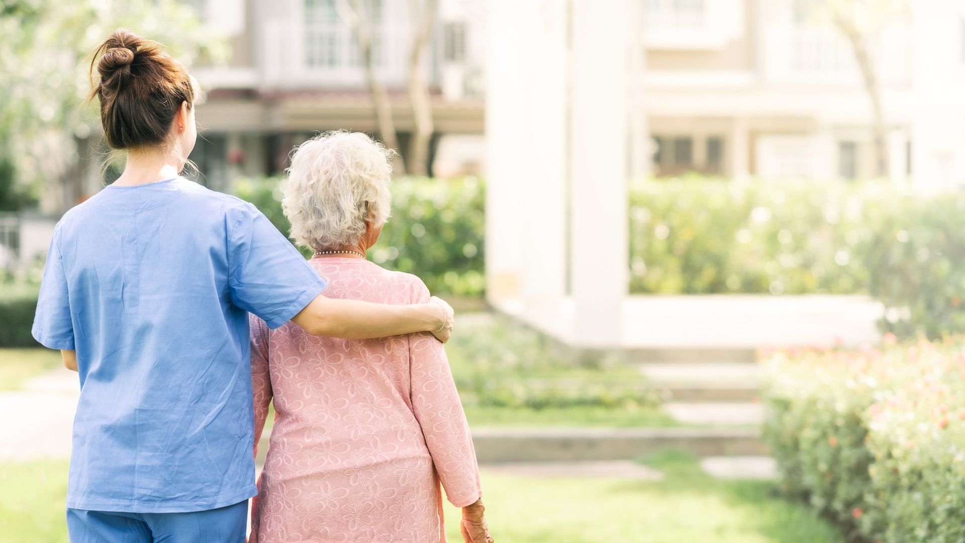 An elderly woman in a wheelchair is being helped by a nurse.